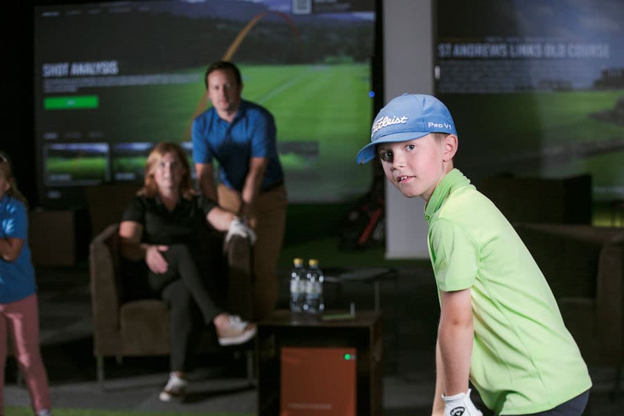 A young golfer lining up a shot in a bay while his family watches