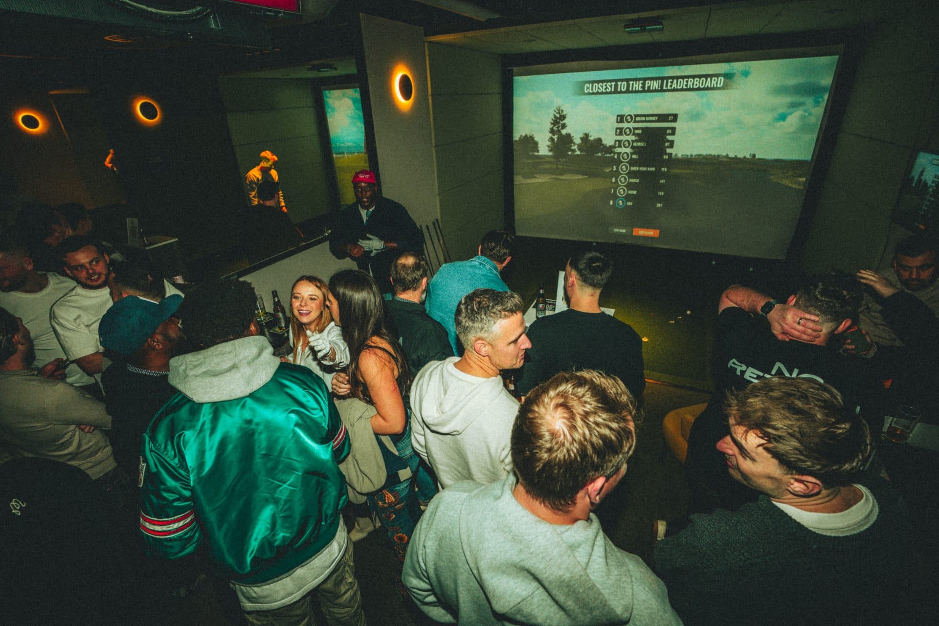 Players gathered in front of a leaderboard on a Caddi Club competition night